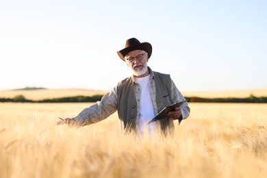 Photo of Senior farmer with clipboard in field of ripe wheat outdoors