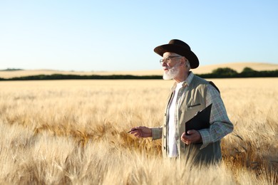 Photo of Senior farmer with clipboard in field of ripe wheat outdoors, space for text