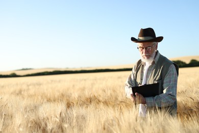 Photo of Senior farmer with clipboard in field of ripe wheat outdoors, space for text