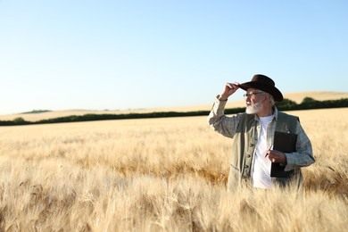 Photo of Senior farmer with clipboard in field of ripe wheat outdoors, space for text