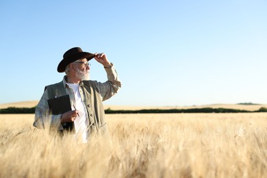 Photo of Senior farmer with clipboard in field of ripe wheat outdoors, space for text