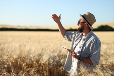Photo of Farmer with tablet in field of ripe wheat outdoors, space for text