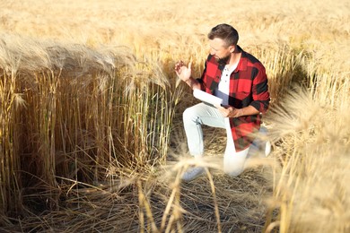 Photo of Farmer with clipboard in field of ripe wheat outdoors, space for text