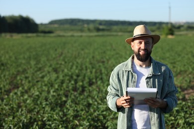 Photo of Farmer with clipboard in field of unripe soy outdoors, space for text