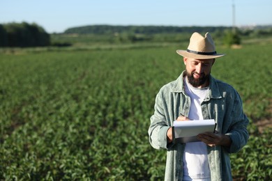Photo of Farmer with clipboard in field of unripe soy outdoors, space for text