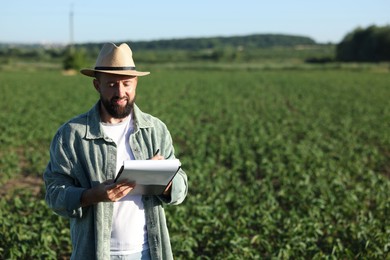 Photo of Farmer with clipboard in field of unripe soy outdoors, space for text