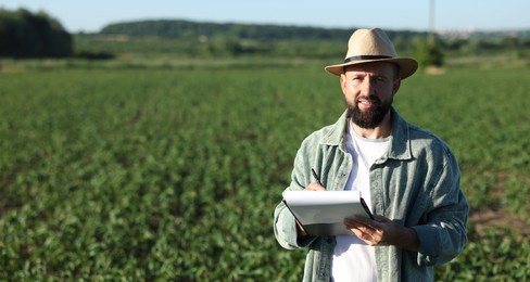 Photo of Farmer with clipboard in field of unripe soy outdoors, space for text
