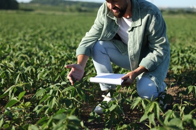 Photo of Farmer with clipboard in field of unripe soy outdoors, closeup