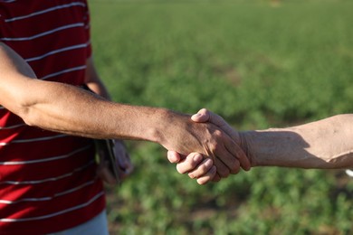 Photo of Farmers shaking hands in field outdoors, closeup