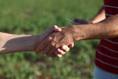 Photo of Farmers shaking hands in field outdoors, closeup