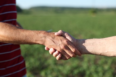 Photo of Farmers shaking hands in field outdoors, closeup