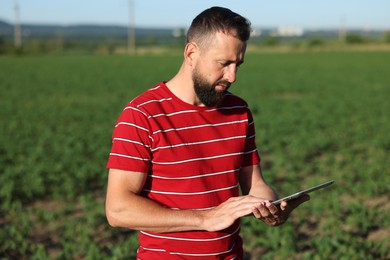 Photo of Farmer with tablet in field of unripe soy outdoors