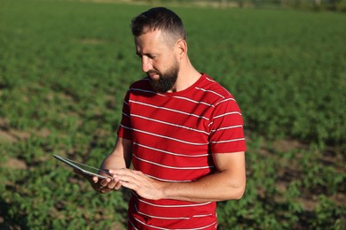 Photo of Farmer with tablet in field of unripe soy outdoors