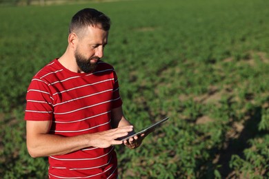 Photo of Farmer with tablet in field of unripe soy outdoors, space for text