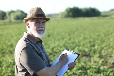 Photo of Senior farmer with clipboard in field of unripe soy outdoors, space for text