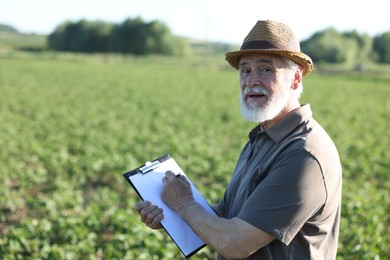 Photo of Senior farmer with clipboard in field of unripe soy outdoors, space for text