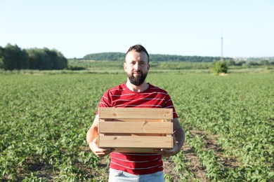 Photo of Farmer with wooden crate in field of unripe soy outdoors