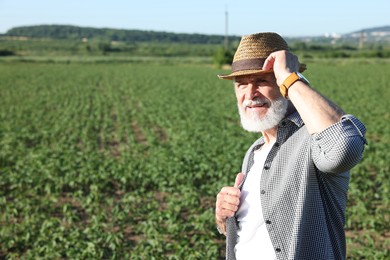 Photo of Senior farmer in field of unripe soy outdoors, space for text