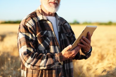Photo of Senior farmer with tablet in field of ripe wheat outdoors, closeup