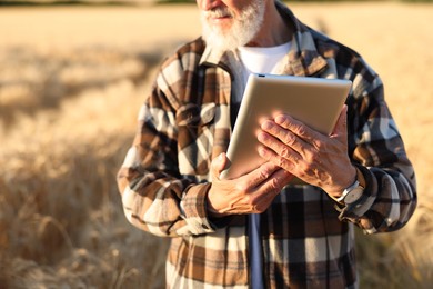 Photo of Senior farmer with tablet in field of ripe wheat outdoors, closeup