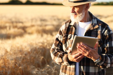 Photo of Senior farmer with tablet in field of ripe wheat outdoors, space for text