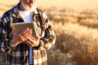 Photo of Senior farmer with tablet in field of ripe wheat outdoors, closeup. Space for text