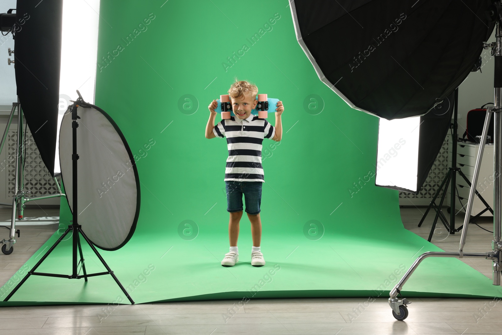 Photo of Little boy with penny board on green background in photo studio with professional equipment