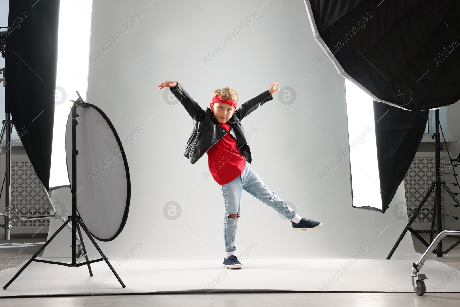 Little boy on light grey background in photo studio with professional equipment Photo of Little boy on light grey background in photo studio with professional equipment