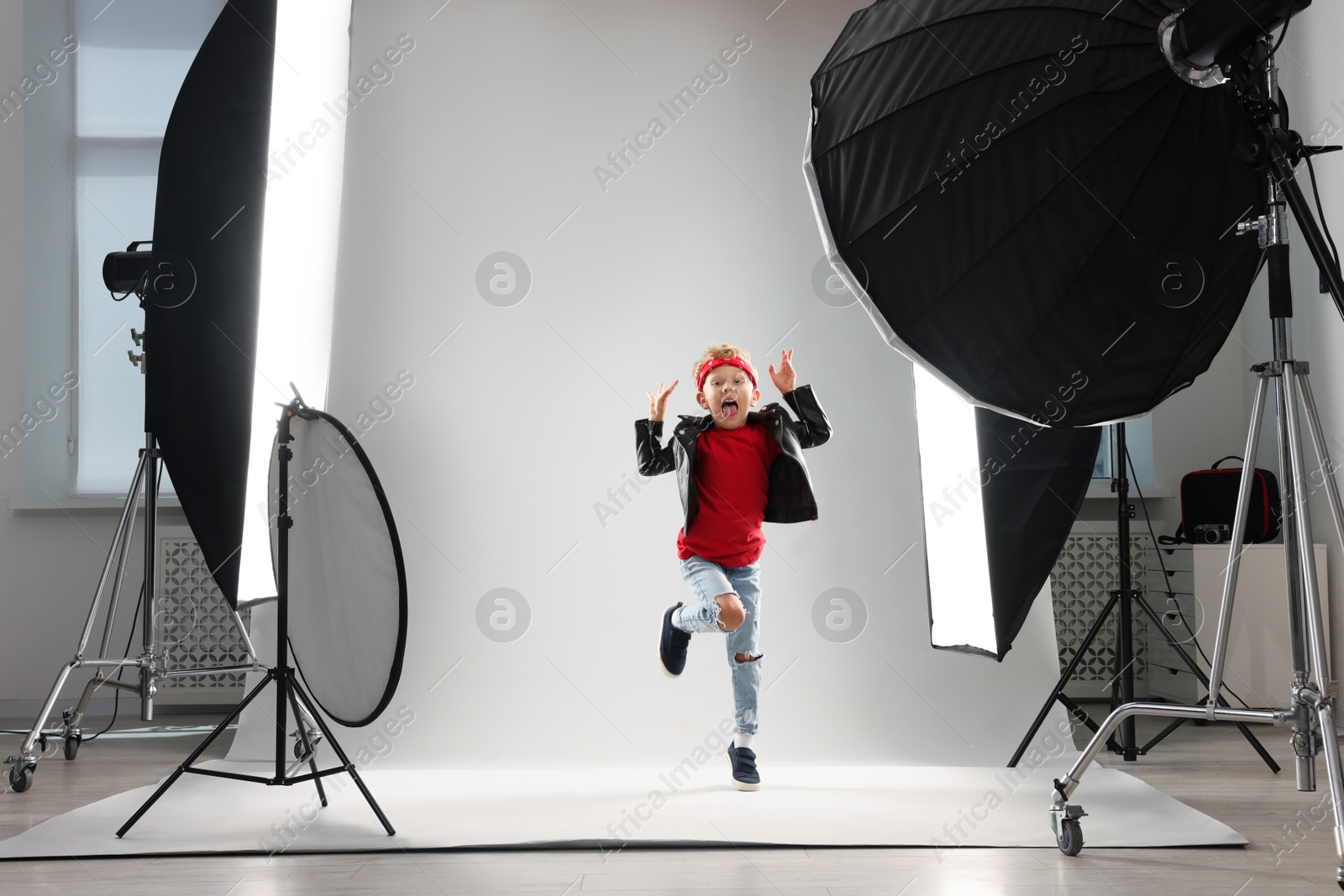 Photo of Little boy on light grey background in photo studio with professional equipment