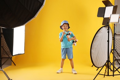 Photo of Little boy with penny board on yellow background in photo studio with professional equipment