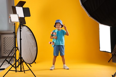 Photo of Little boy with penny board on yellow background in photo studio with professional equipment
