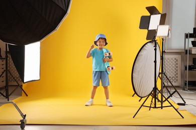 Photo of Little boy with penny board on yellow background in photo studio with professional equipment