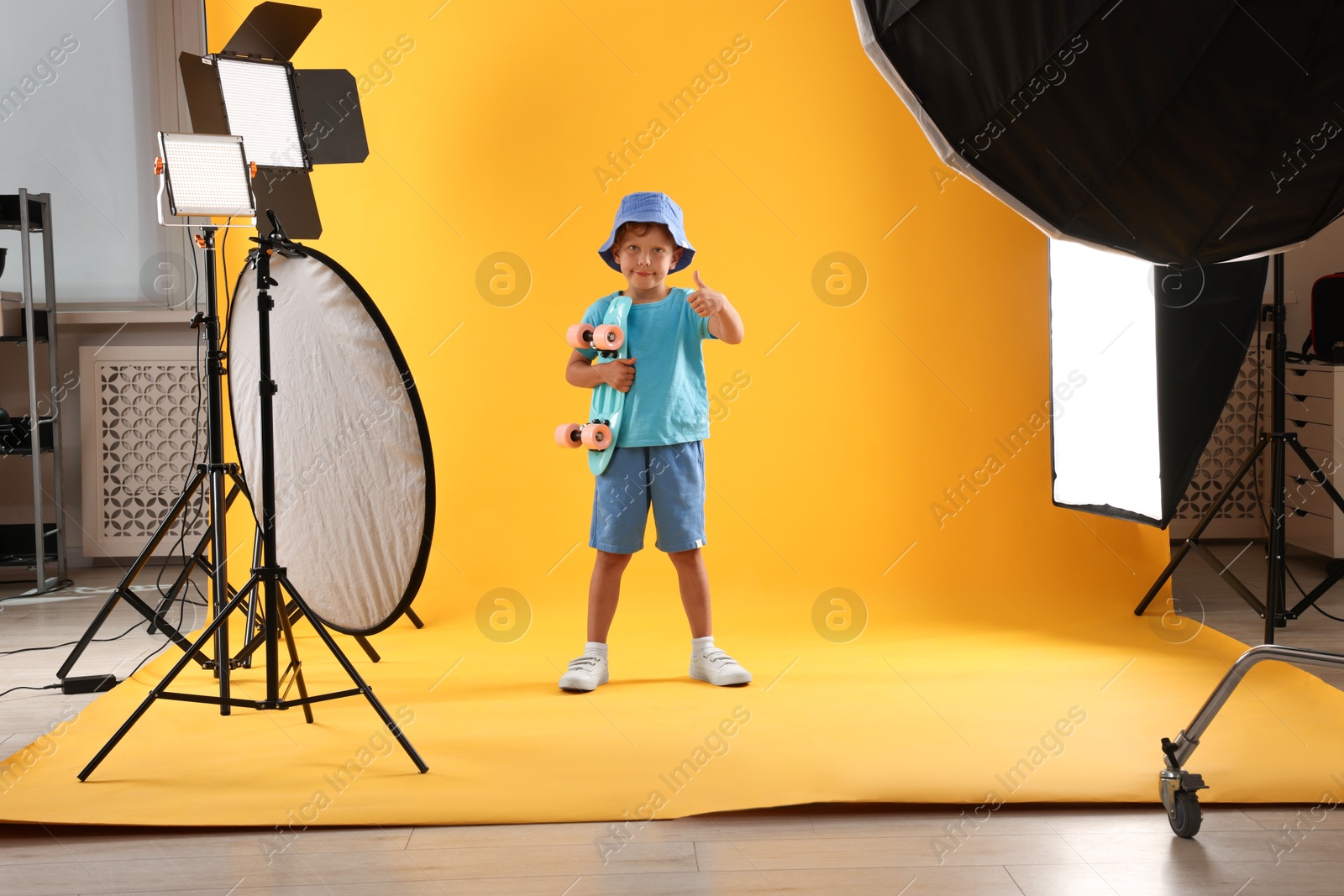 Photo of Little boy with penny board on yellow background in photo studio with professional equipment
