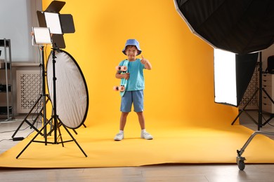 Photo of Little boy with penny board on yellow background in photo studio with professional equipment