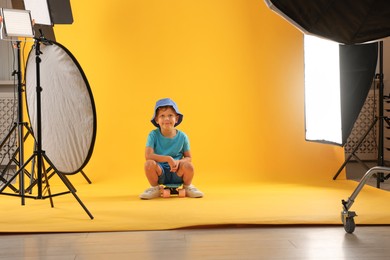 Photo of Little boy with penny board on yellow background in photo studio with professional equipment