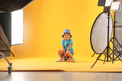 Photo of Little boy with penny board on yellow background in photo studio with professional equipment