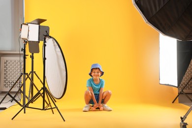 Photo of Little boy with penny board on yellow background in photo studio with professional equipment
