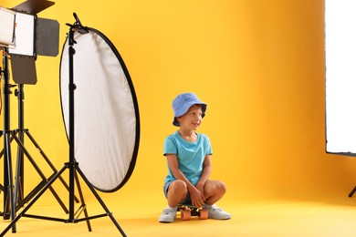 Photo of Little boy with penny board on yellow background in photo studio with professional equipment
