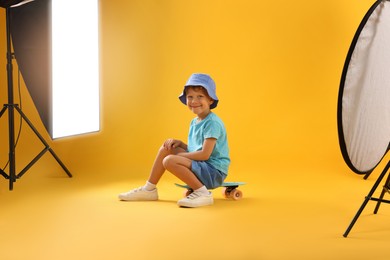 Photo of Little boy with penny board on yellow background in photo studio with professional equipment