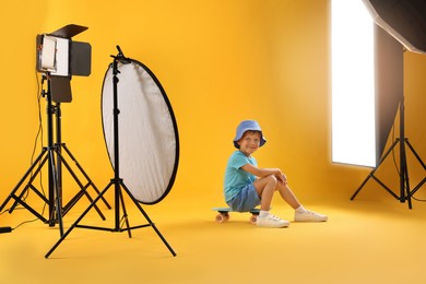 Photo of Little boy with penny board on yellow background in photo studio with professional equipment