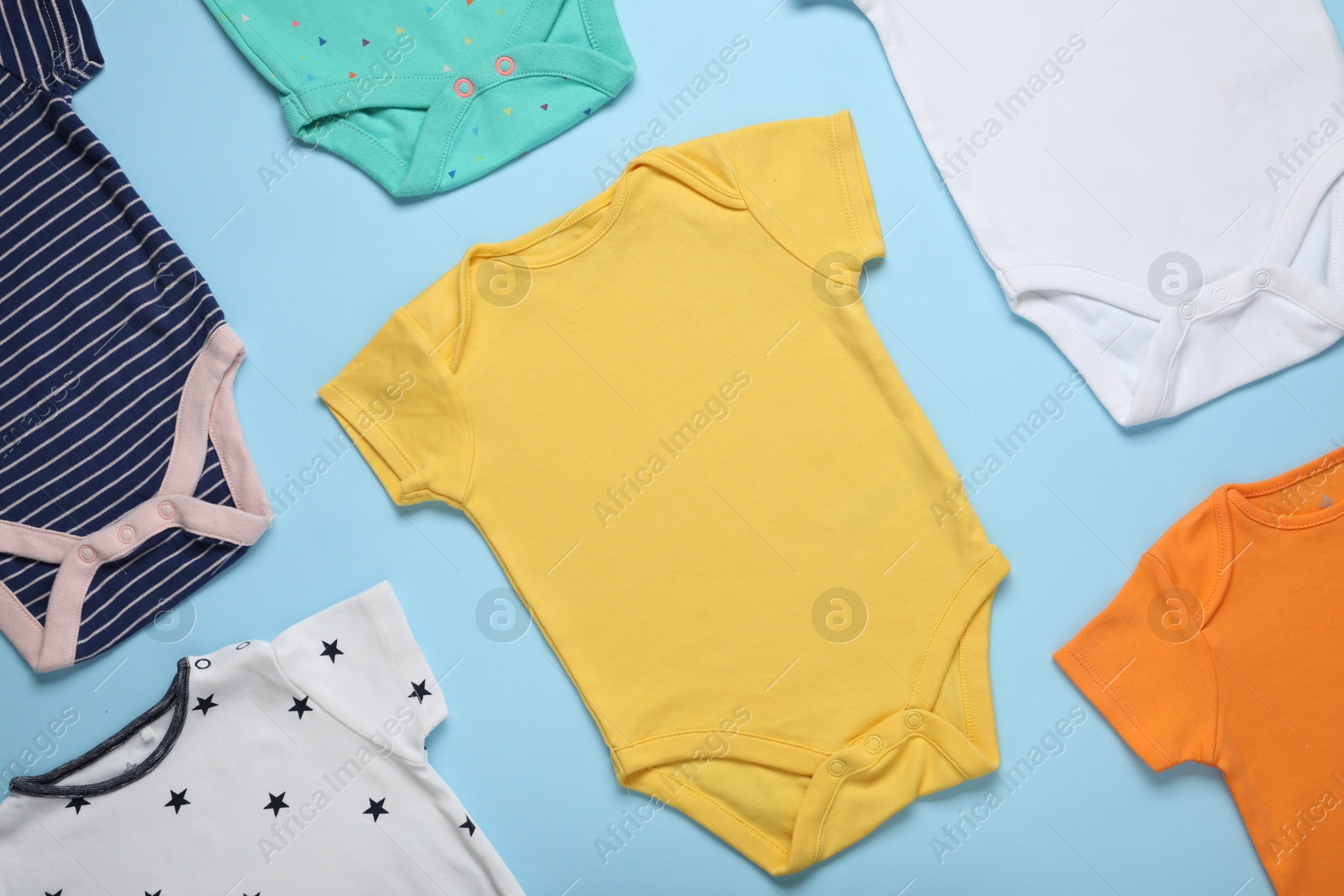 Photo of Different baby onesies on light blue background, flat lay