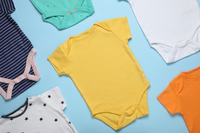 Photo of Different baby onesies on light blue background, flat lay