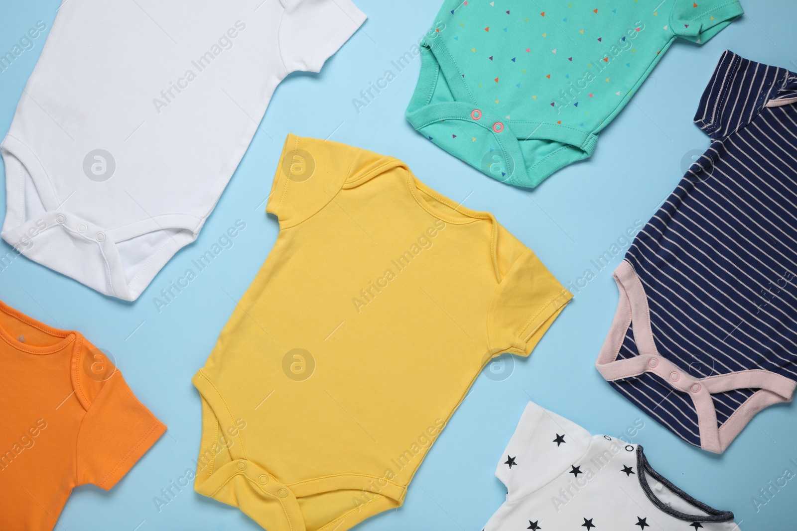 Photo of Different baby onesies on light blue background, flat lay