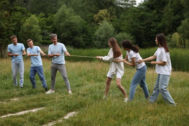 Photo of Team building. Group of happy people playing tug of war with rope outdoors