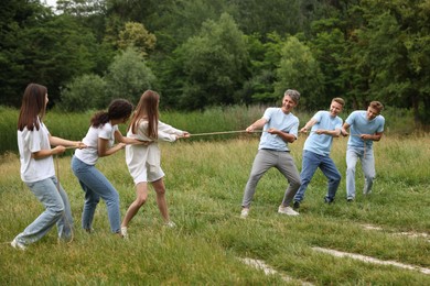 Photo of Team building. Group of happy people playing tug of war with rope outdoors