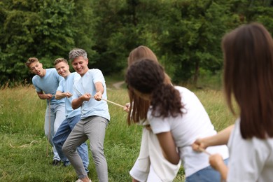 Photo of Team building. Group of happy people playing tug of war with rope outdoors