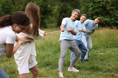 Photo of Team building. Group of happy people playing tug of war with rope outdoors