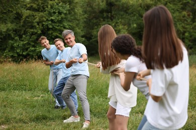 Photo of Team building. Group of happy people playing tug of war with rope outdoors