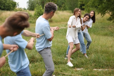 Photo of Team building. Group of happy people playing tug of war with rope outdoors