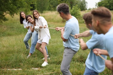 Photo of Team building. Group of happy people playing tug of war with rope outdoors